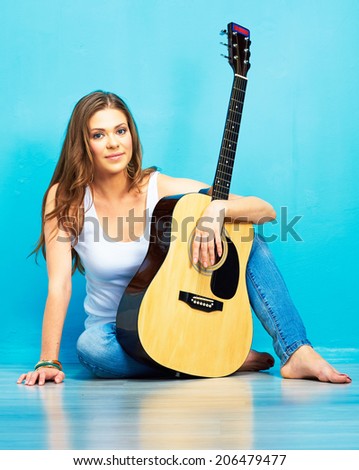Young woman musician with guitar sitting on a floor. Blue background.