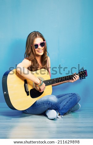 young woman sings and playing guitar . sitting against blue