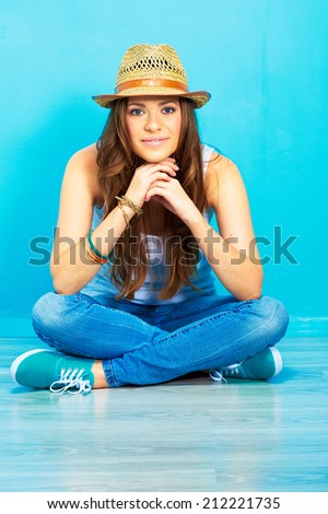 young woman with long curly hair sitting on floor against blue wall . female portrait .  crossed leg