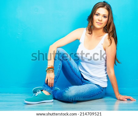 young smiling woman sitting on floor against blue wall . hipster style .