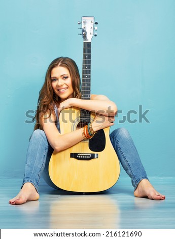 smiling musician girl with acoustic guitar sitting on a floor . 70s style woman portrait with long hair.