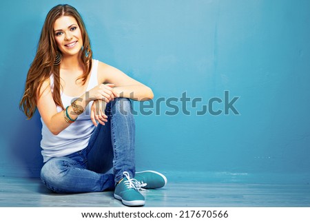 beautiful smiling woman sitting on floor against blue wall . fashion model .