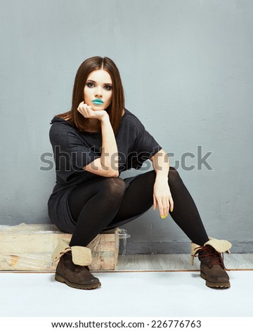 Fashion model with straight hair. Young beautiful woman seat against wall.