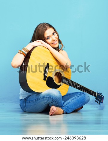 girl with acoustic guitar sitting on a floor against blue. 70s hippie style .