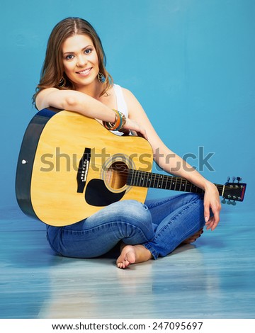 young model girl with acoustic guitar against blue wall background