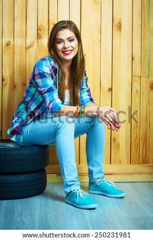 Young woman sitting on auto tires against wooden wall. Smiling model with long hair. Beautiful girl portrait.