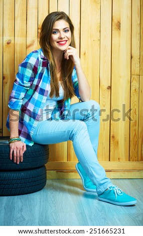 Young woman sitting on auto tires against wooden wall. Smiling model with long hair. Beautiful girl portrait.