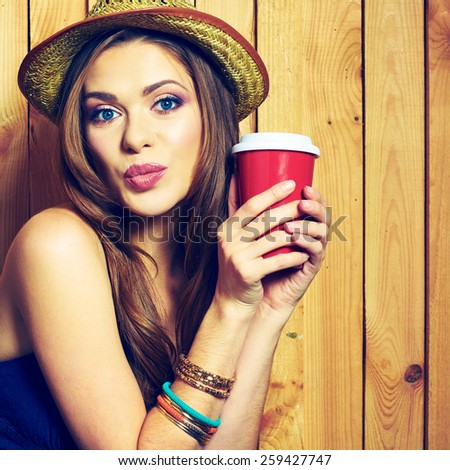 Kissing Hipster Girl Holding Coffee Cup. Yellow hat.Female  model with long hair. Beauty Face Portrait against wooden background.