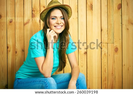 Teenager girl smiling with teeth seating against wood background. Young woman portrait with hat in hipster style.