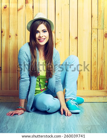Beautiful smiling girl sitting against wooden background on a floor. Youth teen style portrait.