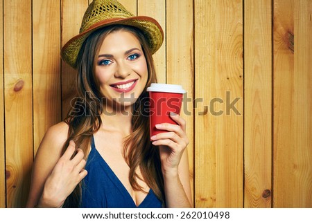 Smiling Young Woman Holding Coffee Cup. Yellow hat. Teeth smiling model with long hair posing on yellow wooden background.