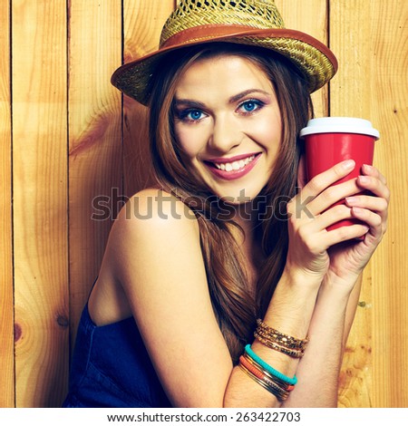 Smiling Hipster Girl Holding Coffee Cup. Yellow hat. Teeth smiling model with long hair.