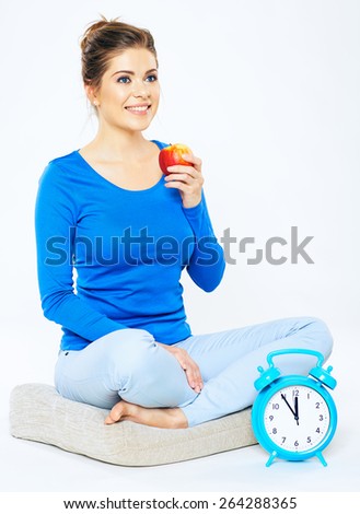 Time for reception of natural vitamins. Concept with alarm clock and red apple. Young woman portrait sitting pose isolated on white background.
