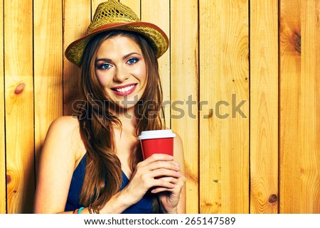 Smiling Hipster Girl Holding Coffee Cup. Yellow hat. Teeth smiling model with long hair.