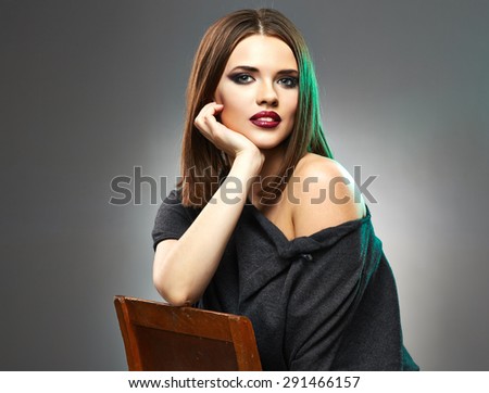 Beautiful woman in black dress sitting on old chair. Studio portrait on gray background.