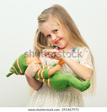 Smiling girl play with doll toy. Isolated portrait of girl with long blond hair.