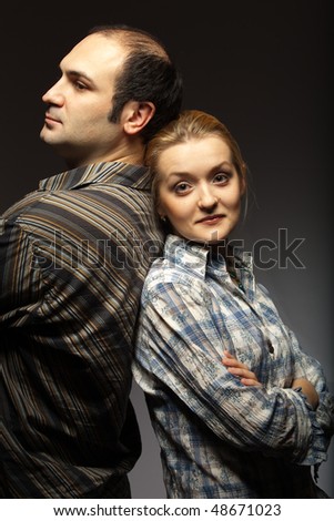 Man and woman stand back to each other against dark background
