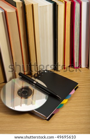 Black notebook ,digital disc and pen near books on table