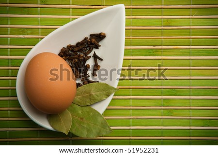 Egg and laurel leaves in a white container in the green bamboo mat
