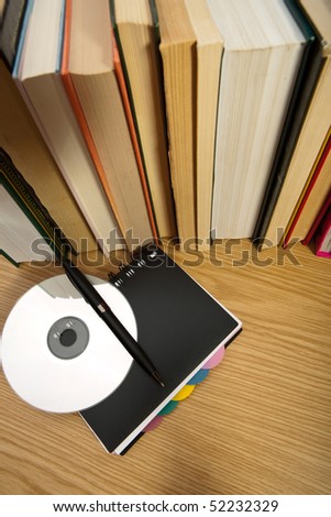 Black notebook ,digital disc and pen near books on table
