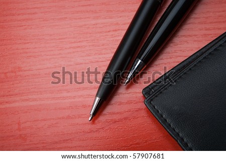 Leather purse lies on a wooden table. Near to purse two pen  lies.