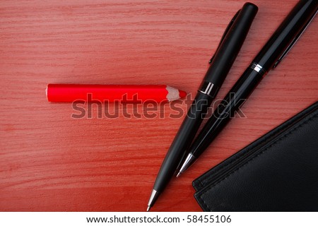 Leather purse lies on a wooden table. Near to purse the pen and pencils lies.