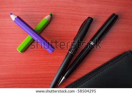 Leather purse lies on a wooden table. Near to purse the pen and pencils lies.