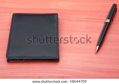 Leather purse lies on a wooden table. Near to purse  pen  lies.