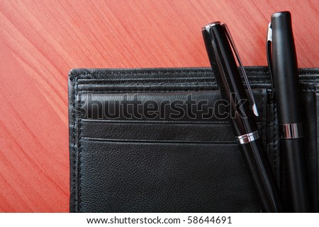 Open leather purse lies on a wooden table. Black pen in a purse.