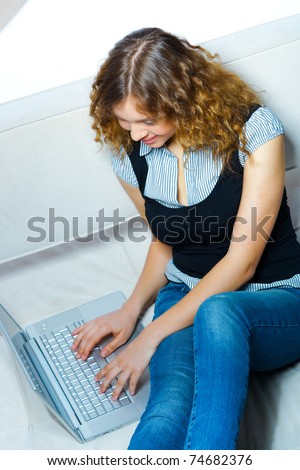 Young woman sitting with  laptop on a couch. Indoor female working portrait