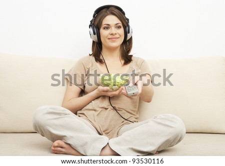 girl watches TV and eats salad. sitting on sofa. headphones on head