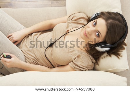 young girl portrait lying on a sofa, listen music in headphones. indoor relax at home. beautiful woman. smiling and happy