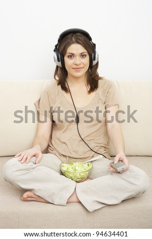 girl watches TV and eats salad. sitting on sofa. headphones on head