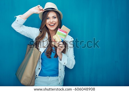 Smiling woman traveler holding passport with ticket and credit card. Blue wall back.