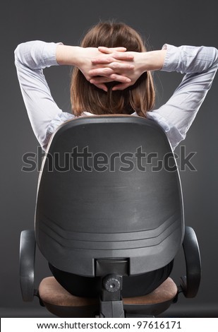 Young business woman [ student ] sits back in office chair isolated on gray