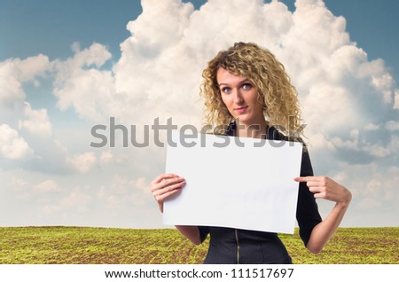 Attractive young business woman with curly hair pointing on blank poster in her hands against rural background.
