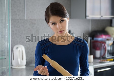 Portrait of young attractive caucasian brunette angry housewife with rolling pin  at kitchen.