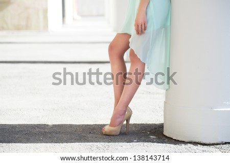 Beautifull long legs of  young woman in soft light green dress standing near the white columns .