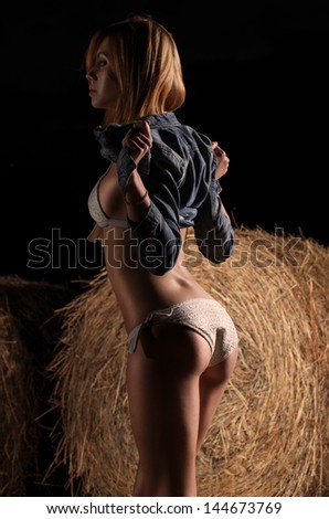 Beautiful young caucasian girl in white bikini and jeans jacket near the haystack at the field.