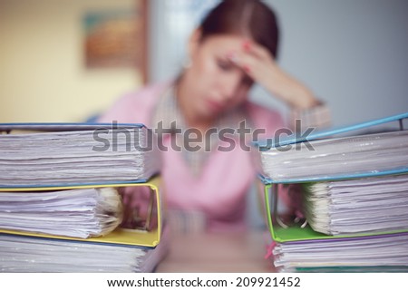 Portrait of young caucasian sad business woman with stacks of ring binders sitting at the desk