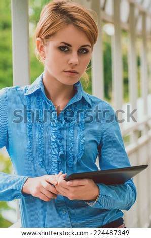 Business woman in a blue striped shirt with tablet pc leaning against the frame of the balcony
