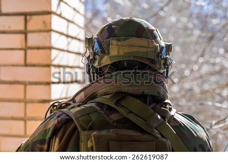 Closeup back view of soldier wearing camouflage helmet with headset radio looking outside