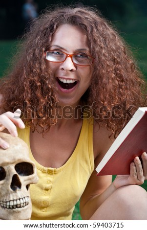?oung women in park with the book and a skull spitefully laughs loudly in the evening