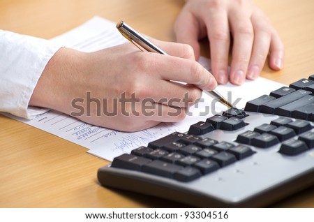Female hand with pan writing on the paper nearkeyboard on the table