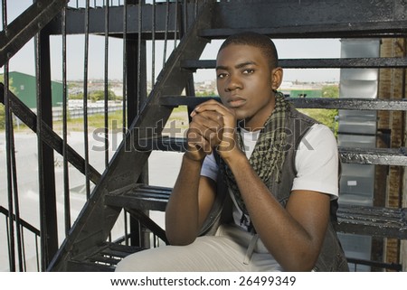 A young African American man sitting in an urban environment.
