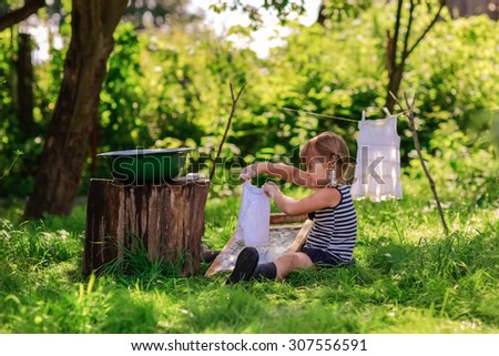 little helper girl washes white dress in a basin outdoors using the washboard outdoors