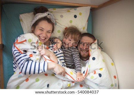 hugging a fun family with son playing in the children\'s bed, hiding under a blanket, casual, lifestyle, real interior, soft focus and light background, toning
