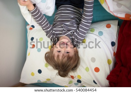 smiling Kid boy lying on the bed with his eyes closed, playing with sleep, lifestyle, real interior, soft focus and light background.