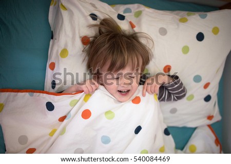 smiling Kid boy lying on the bed with his eyes closed, playing with sleep, lifestyle, real interior, soft focus and light background.