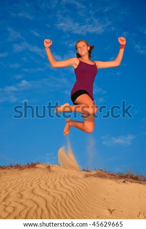 Female jumping off sand dunes with blue sky